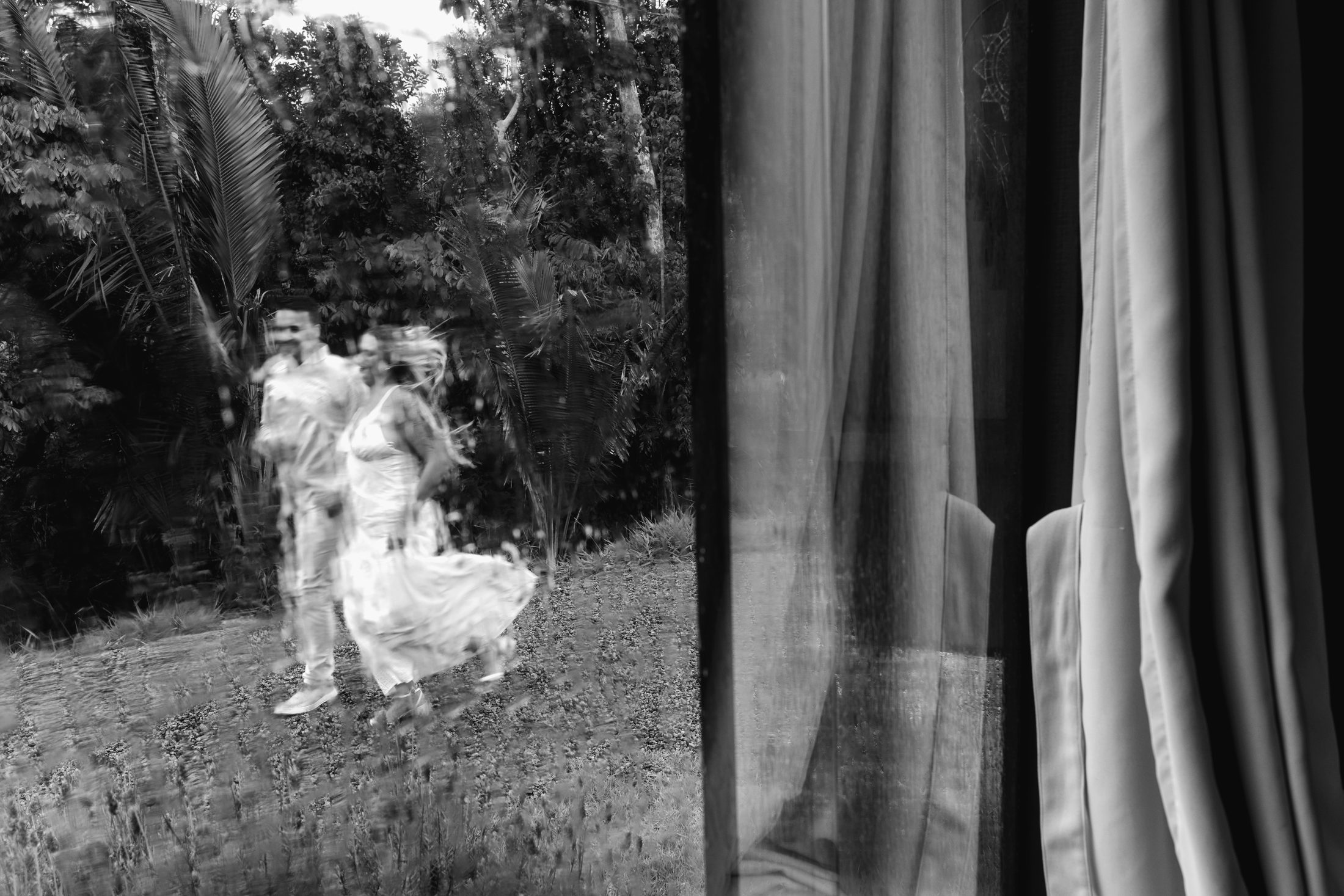 Nadia en Pieter stap deur 'n bos, gesien deur 'n venster